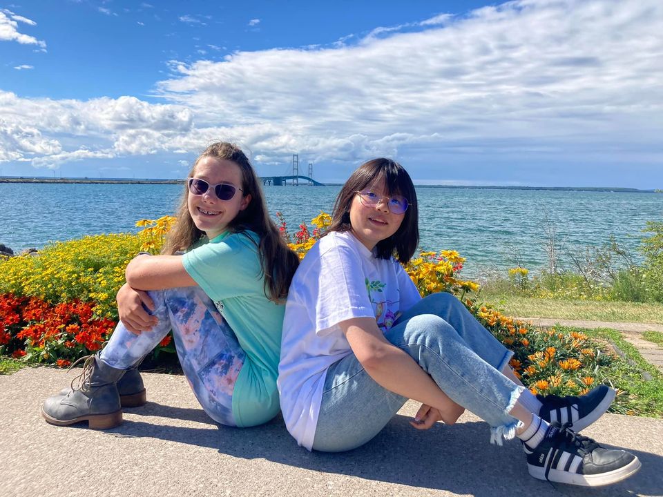 two girls sitting back to back, smiling.